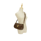Manequim feminino de costura exibindo a Bolsa Baguete Clarissa marrom sendo usada a tiracolo, demonstrando o caimento da alça longa e a proporção da bolsa. Preto Caramelo Off White Marrom