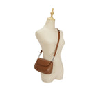 Manequim feminino exibindo a Bolsa Baguete Minimalista Isabele marrom sendo usada a tiracolo, demonstrando a proporção exata e o caimento elegante no corpo. Preto Caramelo Off White Bege