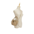 Manequim feminino exibindo a Bolsa Bucket Beatrice bege na transversal, demonstrando o caimento da alça de corrente e a proporção delicada do modelo no corpo. Preto Caramelo Off White Bege