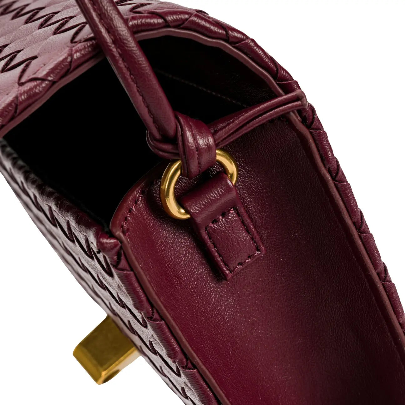 Close-up da costura interna e da argola metálica dourada que fixa a alça fina transversal da bolsa clutch Diana na cor vinho. Preto Bordô