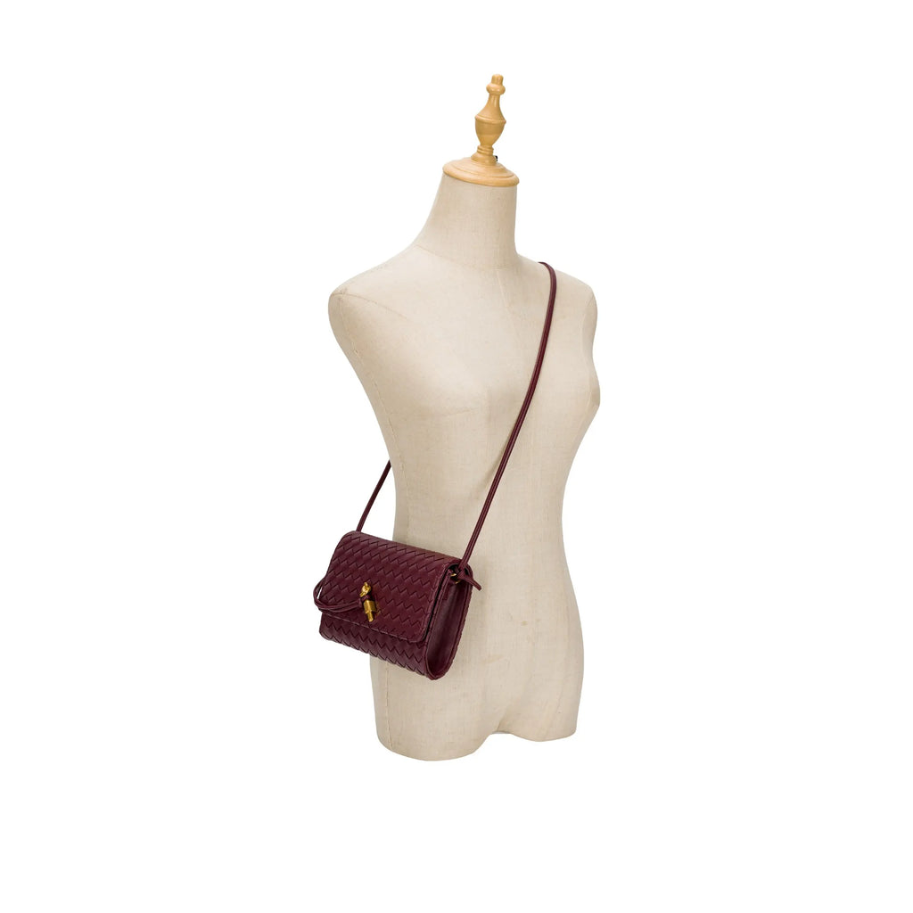 Manequim utilizando a bolsa clutch Diana tressê vinho pendurada com a alça fina transversal (crossbody), demonstrando as proporções e o caimento minimalista no corpo. Preto Bordô