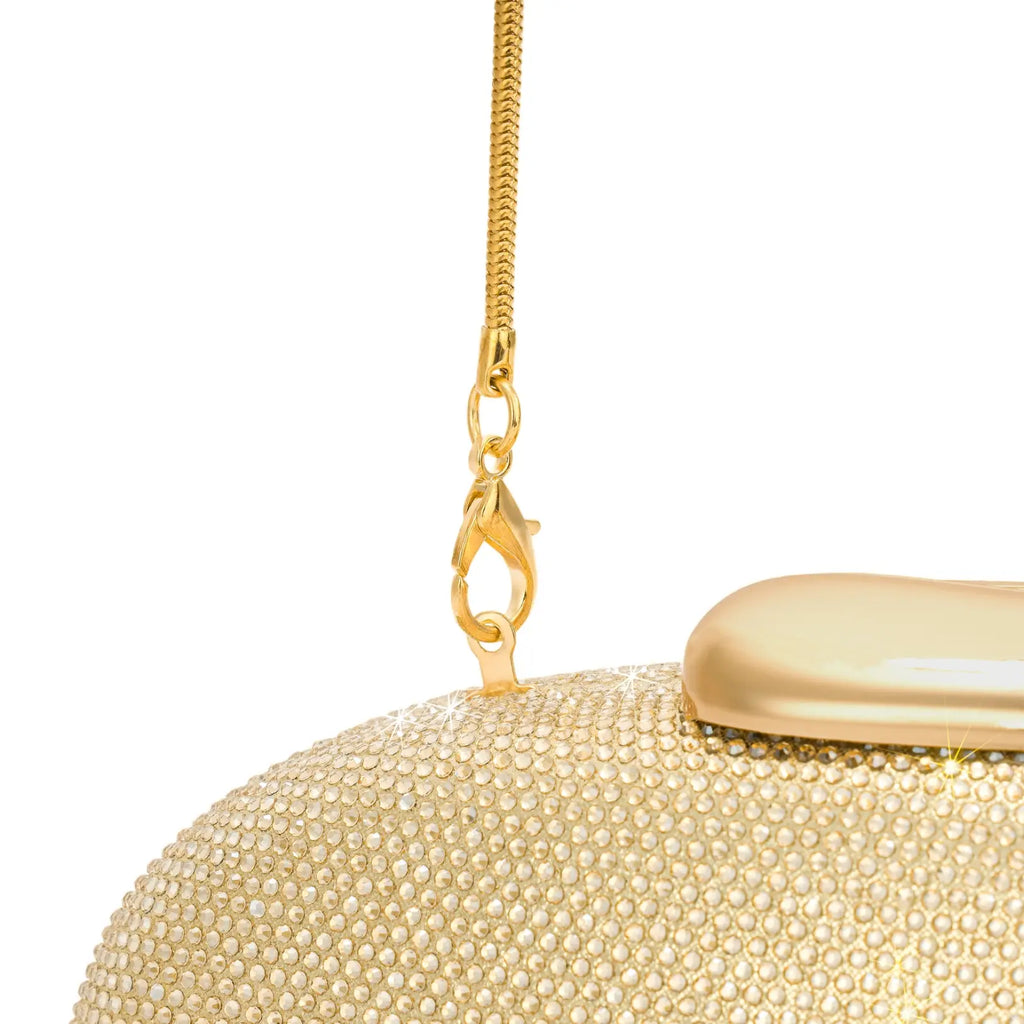 Close-up do mosquetão metálico dourado que prende a alça de corrente fina à argola da bolsa clutch Melissa. Preto Dourado