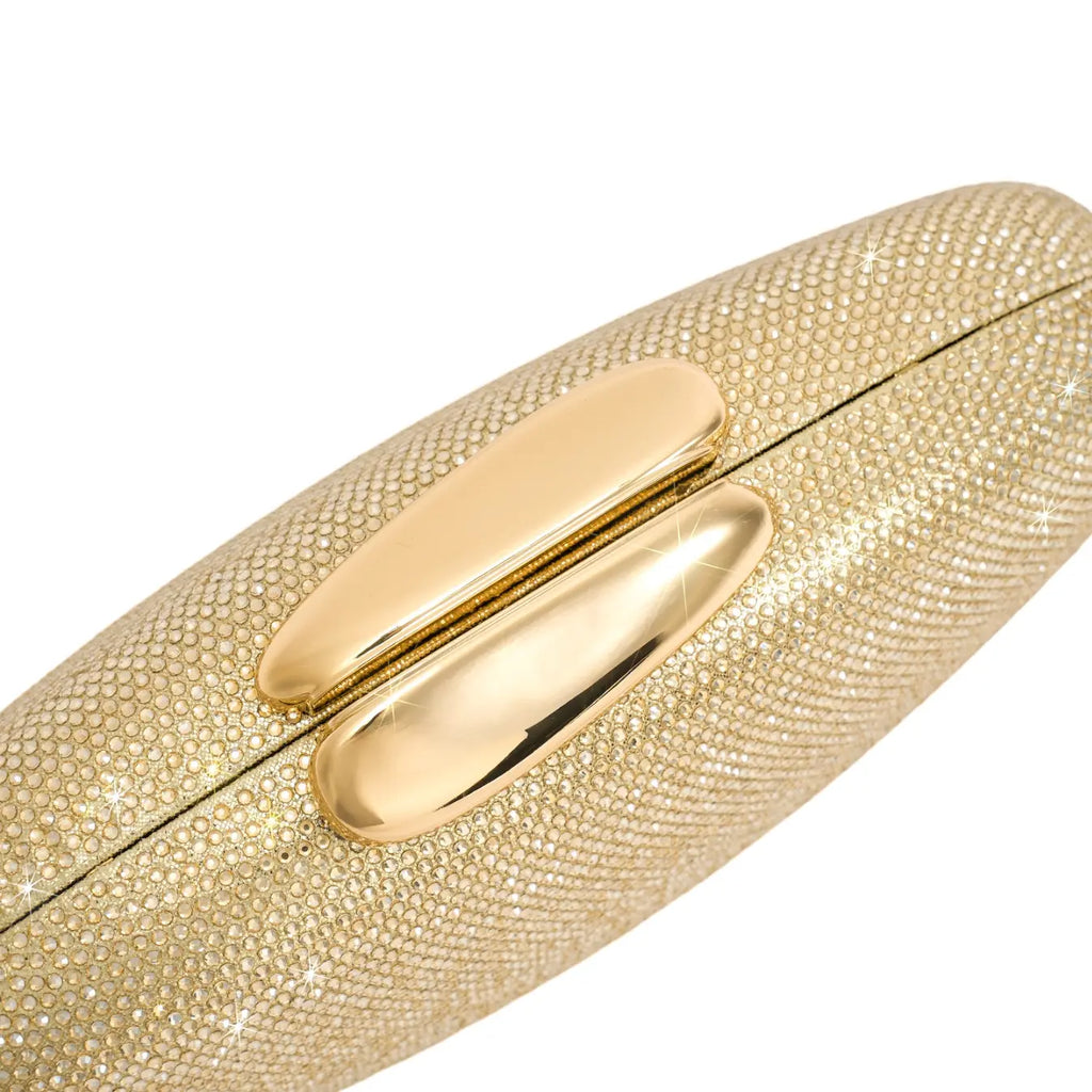 Close-up do fecho superior de encaixe da bolsa clutch Melissa dourada, feito em metal liso e brilhante, contrastando com o corpo cravejado. Preto Dourado