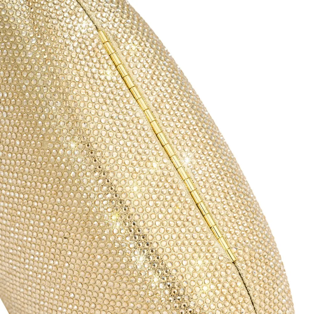 Detalhe em macro da textura inteiramente cravejada de mini cristais da bolsa clutch Melissa dourada e da dobradiça metálica inferior. Preto Dourado