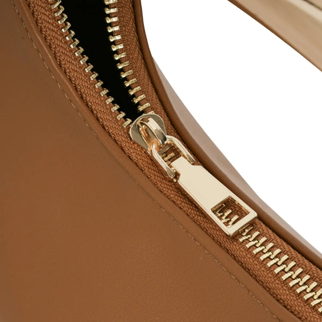 Detalhe aproximado do puxador retangular liso e do trilho do zíper metálico dourado responsável pelo fechamento superior seguro da bolsa hobo meia lua Marianne cor caramelo. Preto Caramelo Off White