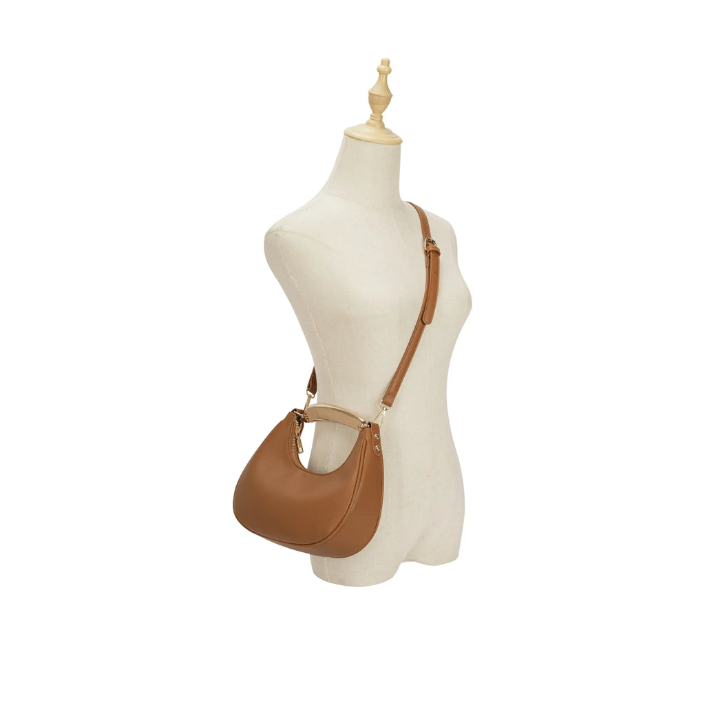 Manequim exibindo a bolsa hobo meia lua Marianne caramelo em uso no estilo transversal (crossbody) com a alça longa, demonstrando a proporção da bolsa e o caimento perfeito no corpo feminino. Preto Caramelo Off White