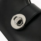 Detalhe em macro do elegante fecho rotativo metálico redondo prateado, que decora e proporciona segurança extra na aba central da bolsa hobo Talessa preta.