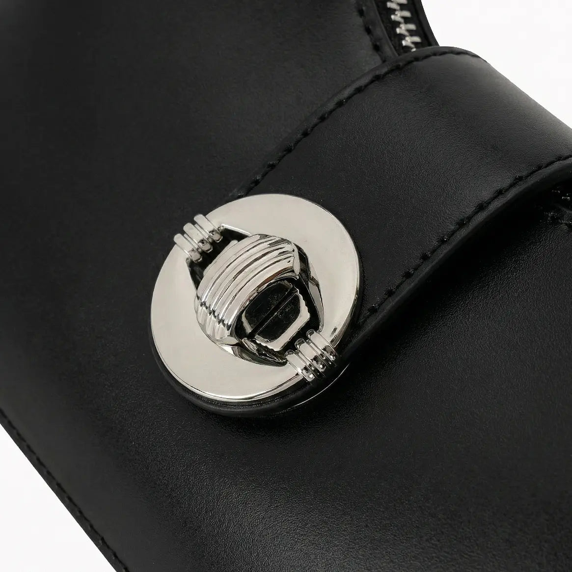 Detalhe em macro do elegante fecho rotativo metálico redondo prateado, que decora e proporciona segurança extra na aba central da bolsa hobo Talessa preta.