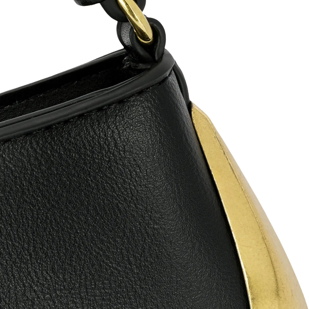 Detalhe aproximado da textura do material preto e da placa metálica lisa dourada que decora e protege a lateral inferior da bolsa mini baguete Catherine. Preto Off White