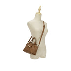 Manequim utilizando a Bolsa Mini Tote Luna marrom a tiracolo, demonstrando o tamanho compacto, o caimento da alça longa e a elegância da peça no corpo. Preto Caramelo Off White