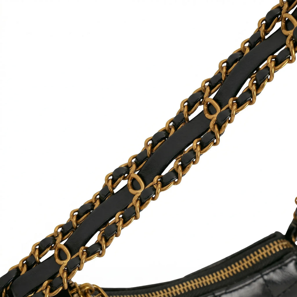 Detalhe aproximado da alça de ombro da Bolsa Amelia composta por tiras de couro preto entrelaçadas em correntes douradas duplas. Preto [cor:Preto]