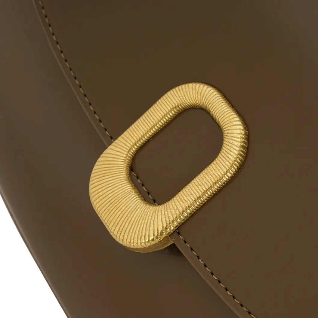 Detalhe em zoom do fecho metálico dourado com acabamento canelado em formato retangular na frente da Bolsa Baguete Clarissa marrom. Preto Caramelo Off White Marrom