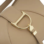 Detalhe em zoom do característico fecho metálico dourado em formato de "D" na frente da Bolsa Hobo Louise bege. Preto Caramelo Off White Bege