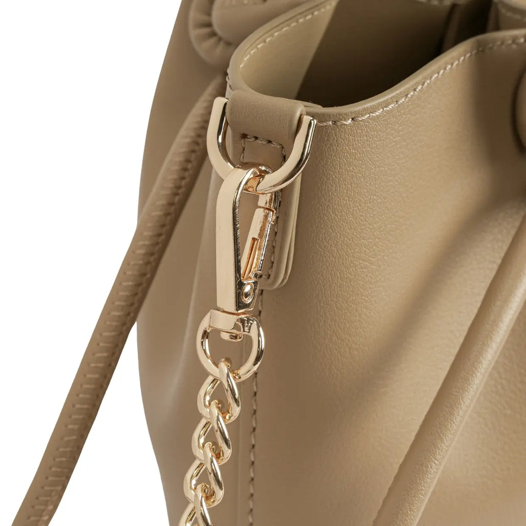 Detalhe em zoom do mosquetão metálico dourado conectando a delicada alça de corrente à argola estruturada da bolsa bege. Preto Caramelo Off White Bege
