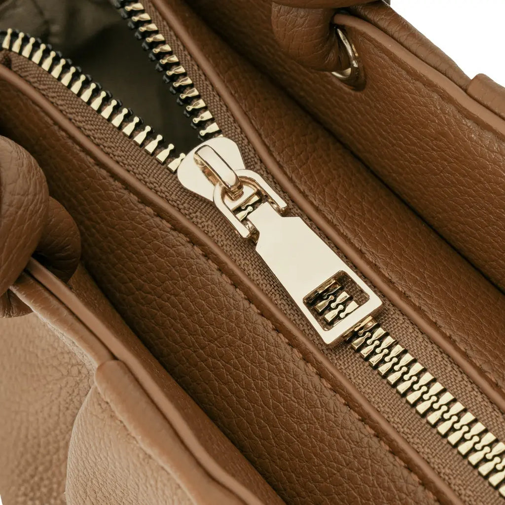 Detalhe aproximado do fechamento superior da bolsa marrom, mostrando o puxador liso do zíper em metal dourado e a textura delicada do couro. Preto Caramelo Off White