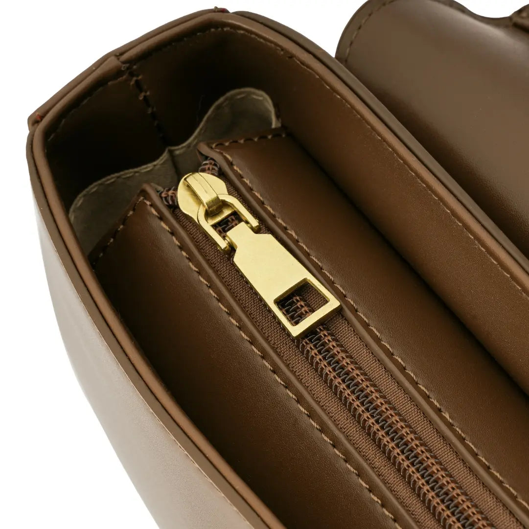 Detalhe macro do acabamento interno da Bolsa Baguete Clarissa marrom, mostrando o puxador do zíper dourado liso e o tecido do forro. Preto Caramelo Off White Marrom