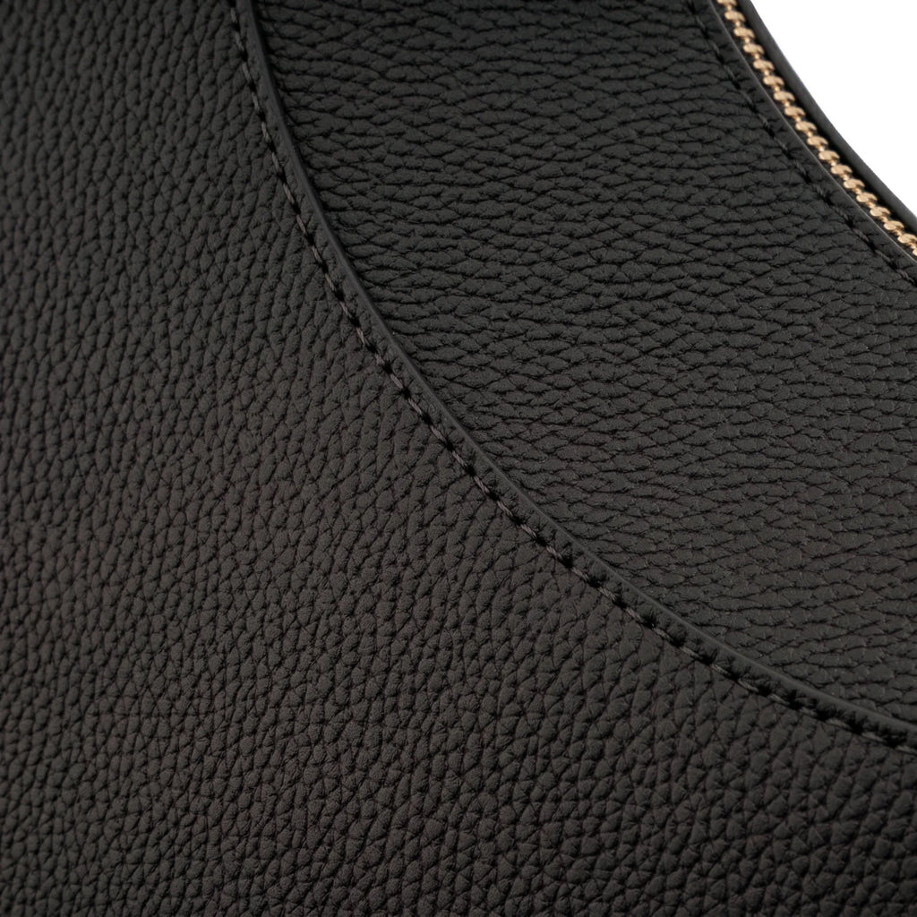 Close-up extremo evidenciando a textura granulada do material e a precisão da costura curva da Bolsa Baguete Victoria preta. Preto [cor:Preto]